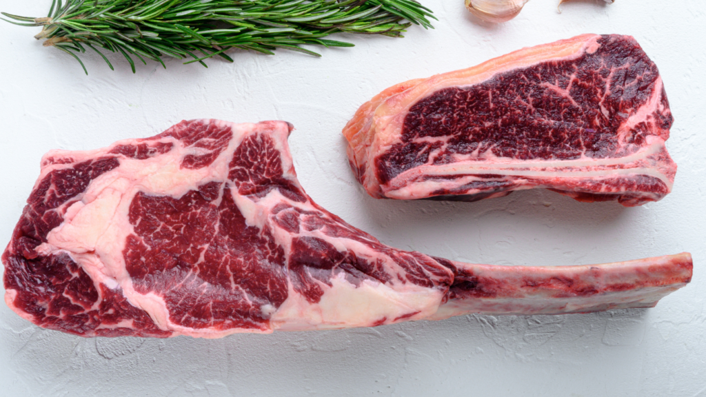 Fresh high-quality beef cuts displayed on a wooden board with herbs and spices, ready for cooking.